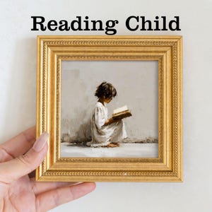 Pu&ograve; includere: Stampa incorniciata con la scritta "Reading Child". L'opera raffigura un bambino in abito bianco intento a leggere un libro. La cornice dorata &egrave; tenuta da una mano su sfondo bianco.