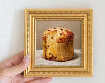 May include: A framed oil painting of a panettone cake. The cake is golden brown with dark spots and a slice cut out. The painting is in a gold frame with a detailed border. The painting is held by a person.