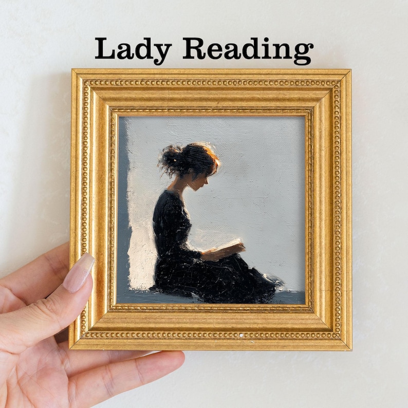 Pu&ograve; includere: Un'opera d'arte incorniciata intitolata "Lady Reading" raffigura una donna in abito nero intenta a leggere un libro. Il dipinto &egrave; ambientato su uno sfondo grigio chiaro, incorniciato in una cornice dorata ornata. La donna ha i capelli rossi.