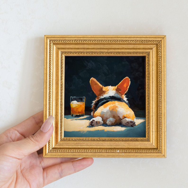 K&ouml;nnte beinhalten: Gerahmtes Gem&auml;lde eines Corgi-Hundes, der von hinten gesehen liegt, mit einem Glas bernsteinfarbener Fl&uuml;ssigkeit. Das Gem&auml;lde befindet sich in einem goldenen Rahmen mit detailliertem Rand. Der Corgi hat orange-wei&szlig;es Fell.