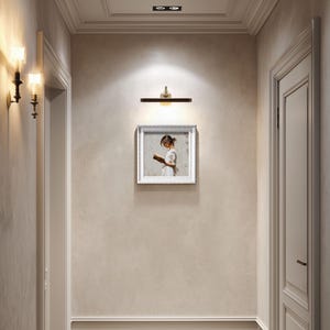 Pu&ograve; includere: Un corridoio con una palette di colori neutri, con un quadro incorniciato di una ragazza che legge, un'applique e un'applique. Il dipinto &egrave; centrato sulla parete, con una porta a destra e una porta a sinistra.