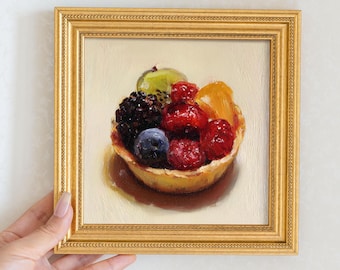 May include: A small, square, framed painting of a fruit tart. The tart is filled with a variety of fresh berries and fruit, including raspberries, blueberries, blackberries, kiwi, and orange slices. The frame is gold-colored.