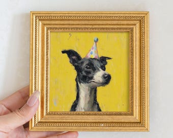 Puede incluir: Pintura enmarcada de un perro blanco y negro con un gorro de fiesta sobre un fondo amarillo. El perro es el punto focal, con una representación detallada de sus rasgos. El marco es dorado.