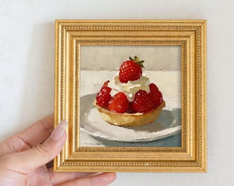 May include: A framed painting of a strawberry tart. The tart features a golden crust, fresh strawberries, and whipped cream, presented on a white plate. The painting is in a gold frame.
