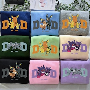 May include: A collection of sweatshirts in various colors, each featuring a graphic design with the letters "D" and "D" in a bold font, along with cartoon characters and the text "EST. 2025". The sweatshirts are folded and stacked.