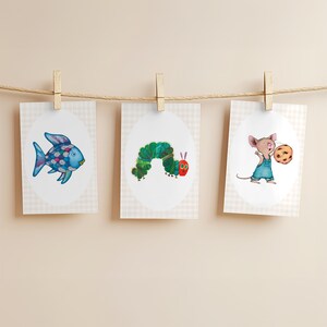 May include: Three illustrated cards hanging from a string with wooden clothespins. The cards feature a blue fish, a green caterpillar, and a mouse holding a cookie. Each illustration is set against a white oval background with a checkered pattern.