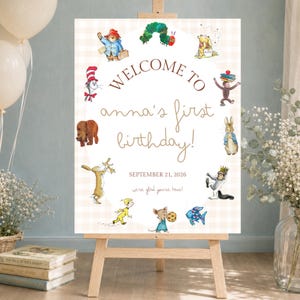 May include: A rectangular welcome sign on a wooden easel featuring a light beige checkered background. The text reads: WELCOME TO anna's first birthday! SEPTEMBER 21, 2026 we're glad you're here! It is decorated with various storybook character illustrations.