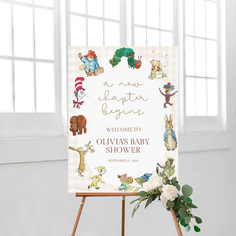 May include: A baby shower welcome sign on a wooden easel. The sign features illustrations of storybook characters and the text "a new chapter begins". The sign welcomes guests to Olivia's baby shower, dated September 21, 2026.