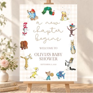 May include: A rectangular sign with a light beige gingham background featuring the text 'a new chapter begins', 'WELCOME TO OLIVIA'S BABY SHOWER', and 'SEPTEMBER 21, 2026'. It is decorated with watercolor illustrations of various storybook characters.