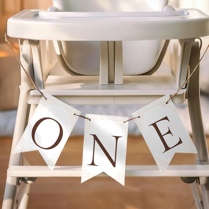 May include: A white high chair with a banner that spells out the word "ONE" in brown letters. The banner is made of white pennant flags with a light brown checkered pattern.