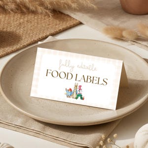 May include: A folded white card with a light pink gingham border featuring the text fully editable FOOD LABELS in brown font. Below the text are small watercolor illustrations of Paddington Bear, Peter Rabbit, and The Cat in the Hat.
