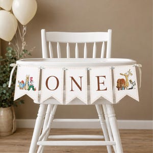 May include: A white high chair features a decorative banner with five pennants. The center three pennants display the brown letters O, N, and E. The outer pennants feature colorful illustrations of various storybook characters.