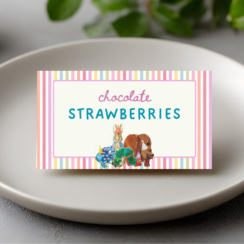 May include: A rectangular food label card featuring a pastel vertical striped border and the text chocolate STRAWBERRIES in pink and blue. The center displays a watercolor illustration of a rabbit, a fish, a caterpillar, and a brown bear.