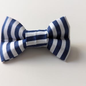May include: A blue and white striped bow tie. The bow tie is made of fabric and has a classic shape. The stripes are evenly spaced and run horizontally across the bow tie.