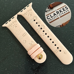 May include: Two pink Apple Watch bands featuring a paw print and "meow" design. The bands are made of silicone and have a buckle fastening.