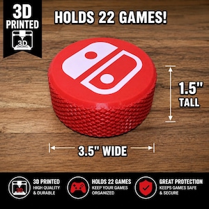 May include: A red 3D printed circular game cartridge holder featuring a white controller icon on top. The holder is 3.5 inches wide and 1.5 inches tall, with a textured diamond pattern on the sides. Text on the image states it holds 22 games.