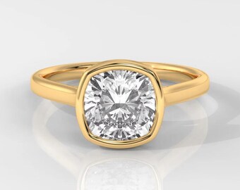 Könnte beinhalten: Ein goldener Ring mit einem großen, quadratisch geschliffenen Diamanten. Der Diamant ist in einer Lünettenfassung gefasst, und das Band ist aus poliertem Gold. Der Ring wird auf einer weißen Oberfläche mit einer darunter sichtbaren Reflexion präsentiert.