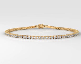 May include: A gold tennis bracelet with a row of small, clear gemstones. The bracelet is set against a white background, showcasing its delicate design and sparkle. The clasp is visible, indicating the bracelet's secure closure.