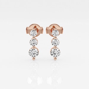 May include: A pair of rose gold earrings, each with three clear, round gemstones in a descending arrangement. The earrings have a post and back, set against a white backdrop.