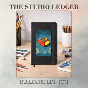 Peut inclure: Cahier noir avec une illustration de bloc coloré sur la couverture. Le texte "THE STUDIO LEDGER" et "BUILDERS EDITION" sont affichés au-dessus et en dessous du cahier. Des pinceaux, des crayons et des fournitures d'art sont disposés autour du cahier.