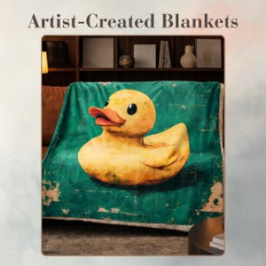 Op de afbeelding: Een deken met een grote gele badeend op een teal achtergrond. De deken heeft een gedetailleerde illustratie van een klassiek badeendje. De woorden "Artist-Created Blankets" staan bovenaan de afbeelding.