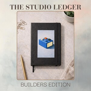 May include: Black notebook with a rectangular image of a blue toy block with colorful studs. The text "THE STUDIO LEDGER" is at the top, and "BUILDERS EDITION" is at the bottom. A gold pen and paper clips are also visible.