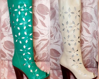 Puede incluir: Dos botas hasta la rodilla con puntera abierta y diseños florales recortados. Una bota es verde turquesa, la otra es blanquecina. Ambas tienen suelas y tacones de plataforma marrones. Las botas son de cuero y tienen una cremallera lateral.