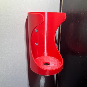 May include: A red plastic wall mount holder with two screws. The holder has a round opening at the bottom.