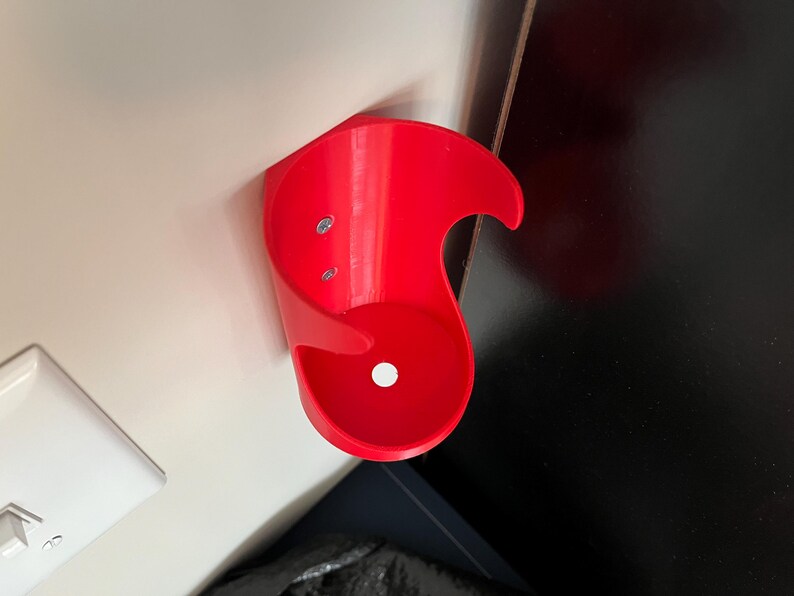 May include: A bright red plastic wall mount cup holder with two screw holes. The holder is designed to hold a single cup or bottle.