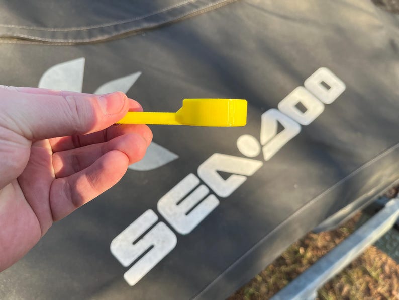 Puede incluir: Una pieza de pl&aacute;stico amarillo brillante con una cabeza rectangular y un mango fino y plano. La pieza se sostiene en una mano, con el fondo que muestra una superficie gris oscuro con el texto blanco "SEA 400".