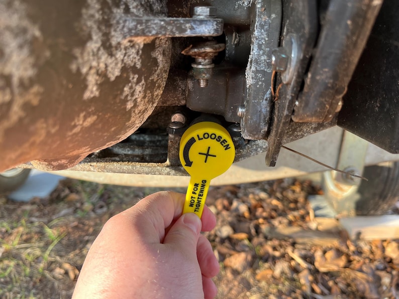 Puede incluir: Una herramienta amarilla con la palabra "LOOSEN" y un s&iacute;mbolo de flecha se sostiene cerca de un componente met&aacute;lico. La herramienta tambi&eacute;n tiene el texto "NOT FOR TIGHTENING". El fondo muestra partes de un veh&iacute;culo.
