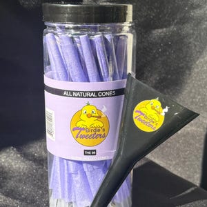 Peut inclure: Un pot transparent rempli de cônes pré-roulés violets, avec l'inscription "All Natural Cones". L'étiquette présente un canard de dessin animé fumant. Un entonnoir noir est à côté.