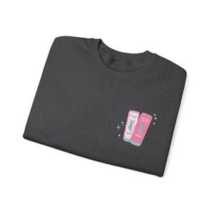 May include: Dark gray sweatshirt featuring a small graphic of two energy drink cans. One can is pink and the other is striped pink and white. The cans have the text "Always Energy" and "Cotton Candy" and "Pink Rush".