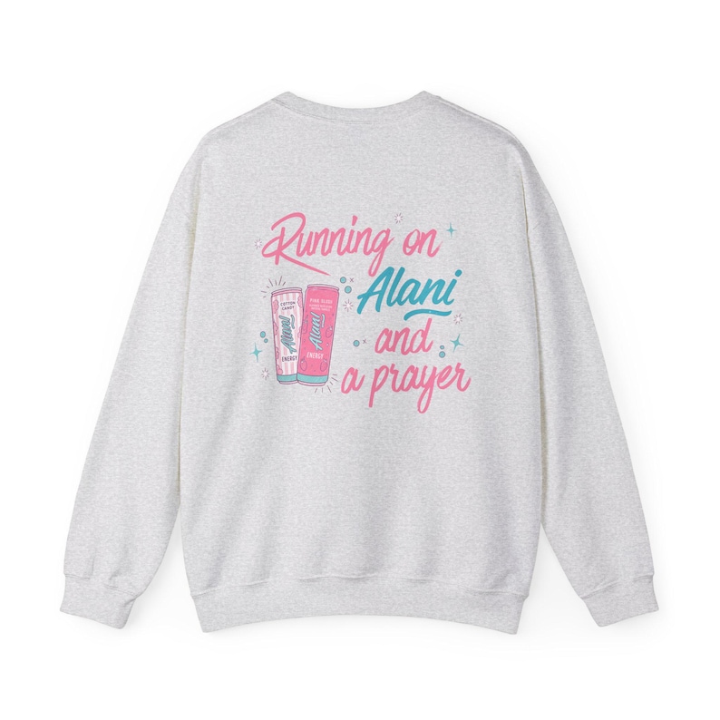 May include: A light gray sweatshirt with the phrase "Running on Alani and a prayer" in pink and teal lettering. The design includes illustrations of two Alani Nu energy drink cans.
