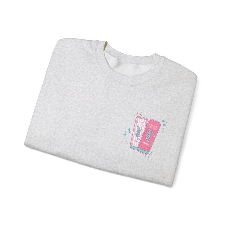 May include: A light gray sweatshirt with a crew neck. The sweatshirt features a small graphic of two energy drink cans, one pink and one light pink, with the text "Alani" and "Energy". The design includes blue and green starburst accents.