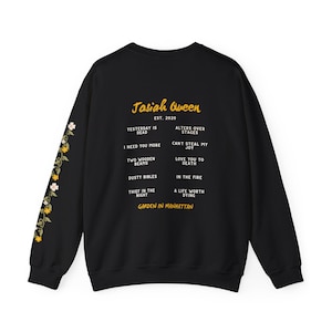 May include: Black sweatshirt with floral sleeve detail. The back features the text "Jasiah Queen EST. 2020" and song titles like "Yesterday is Dead" and "Love You to Death". The phrase "Garden in Manhattan" is also printed on the sweatshirt.