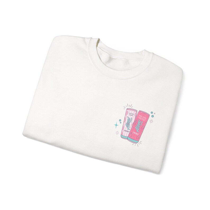 May include: White crew neck sweatshirt with a small graphic of two soda cans. The cans are pink and blue with the text "Always" and "Energy". The design includes stars and sparkles.