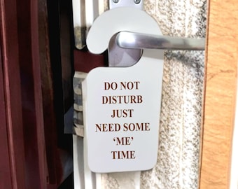 Könnte beinhalten: Ein weißer Türhänger mit dem Text "DO NOT DISTURB JUST NEED SOME 'ME' TIME" in braunen Buchstaben. Der Hänger ist an einem silbernen Türgriff befestigt und hängt an einer Tür mit Streifenmuster.
