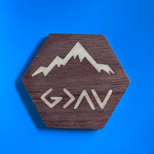 Puede incluir: Un hexágono de madera con un diseño de cordillera y la palabra "G>AV" en color claro. El fondo es azul liso.