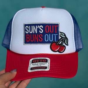 Puede incluir: Gorra de camionero roja, blanca y azul marino con el texto "SUN'S OUT BUNS OUT". La gorra presenta un parche de cereza y una parte trasera de malla.