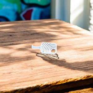 May include: A white plastic key with a unique design featuring a series of concentric circles. The key is lying on a wooden surface.