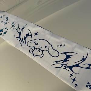 Op de afbeelding: Een rol wit vinyl stickerpapier met een blauw stripfiguur, sterren en tribale ontwerpen. Het stickerpapier heeft een rasterpatroon op de achterkant.