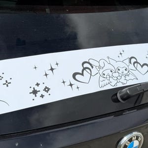 Puede incluir: Calcomanía blanca para coche con una ilustración en blanco y negro de dos personajes de dibujos animados, corazones y estrellas. La calcomanía está aplicada en la luneta trasera de un vehículo negro.