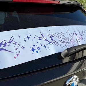 Puede incluir: Una pegatina blanca para la ventana del coche con un diseño tribal morado y azul, estrellas y personajes de dibujos animados. La pegatina está en la ventana trasera de un coche negro.