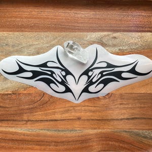 Puede incluir: Un diseño de tatuaje tribal negro con una forma de corazón en el centro. El diseño está en una lámina de plástico transparente.