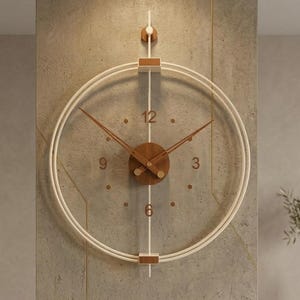Puede incluir: Un reloj de pared moderno con un diseño minimalista. Cuenta con un marco blanco circular con manecillas e indicadores de hora marrones. El reloj está montado en una pared gris texturizada, creando una estética simple pero elegante.