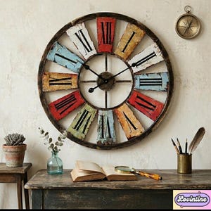 May include: Large, round wall clock with a distressed, multi-colored face and Roman numerals. The clock has a dark brown metal frame and black clock hands. The clock is mounted on a light-colored wall. A vintage-style compass hangs above the clock.