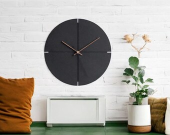May include: A black round clock with four wooden arms and copper-colored hands against a white brick wall.