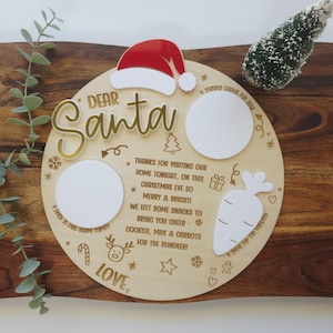 May include: A wooden Christmas Eve serving board with the words "Dear Santa" in gold script. It features a Santa hat, two white circles, and a carrot shape. Text includes "Cookies, Milk & Carrots for the Reindeer!" and "Love".