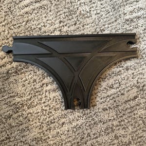 May include: Black plastic train track piece with a Y-shaped design. The track piece has two straight sections and one curved section.